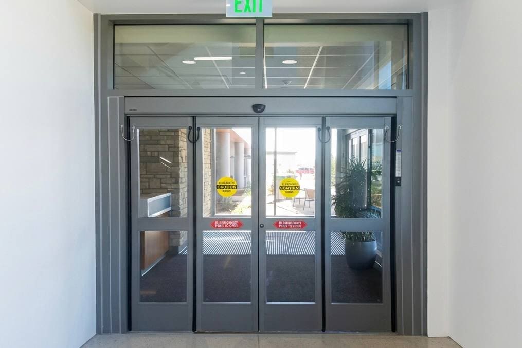 Commercial automatic sliding entrance with an overhead operator and door safety signage